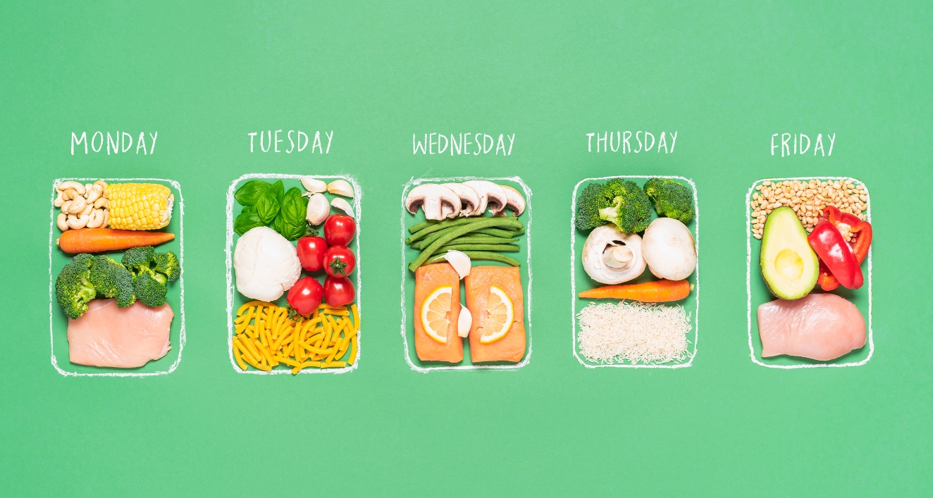 A weekly meal plan layout on a green background. Five containers labeled Monday to Friday show different healthy meal combinations including vegetables, fruits, meats, and grains. Each day features a balanced variety of foods such as broccoli, corn, chicken, pasta, tomatoes, oranges, mushrooms, rice, avocado, and bell peppers.