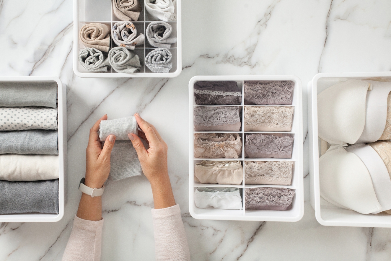 Home organization techniques showcased with neatly folded towels and linens in white storage containers on a marble surface.