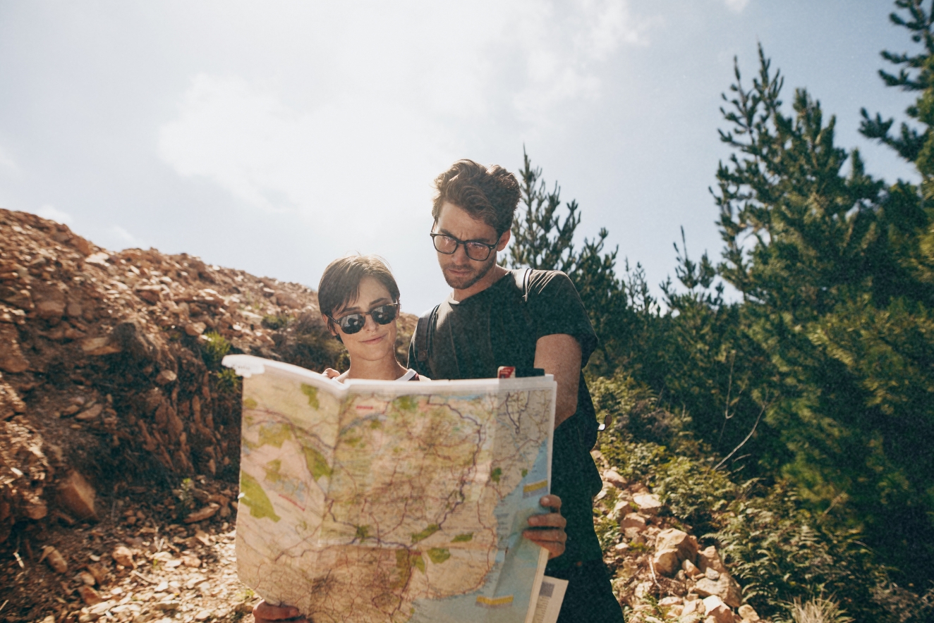 A couple engaged in sustainable travel practices, reading a paper map together while hiking in a natural, mountainous landscape.