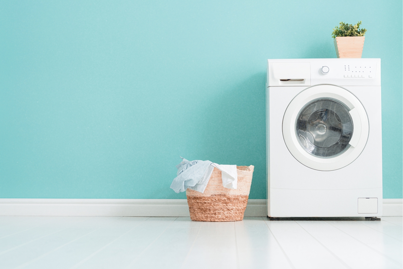 Home organization in a laundry room with a clean white washing machine, neatly arranged laundry basket, and minimalist decor against a teal wall.