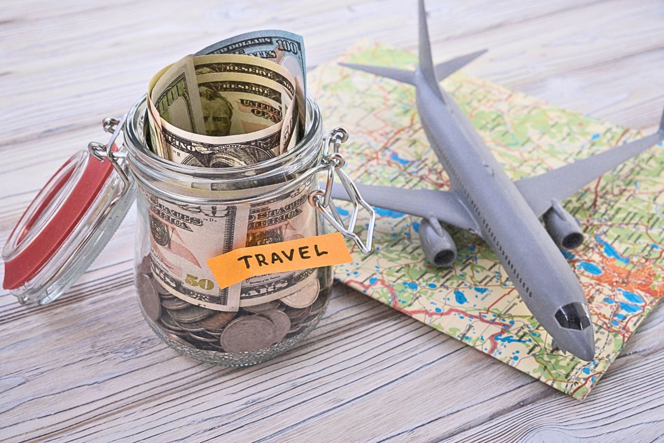 Travel savings jar with cash next to a map and miniature airplane, illustrating budget travel planning and low airfare.