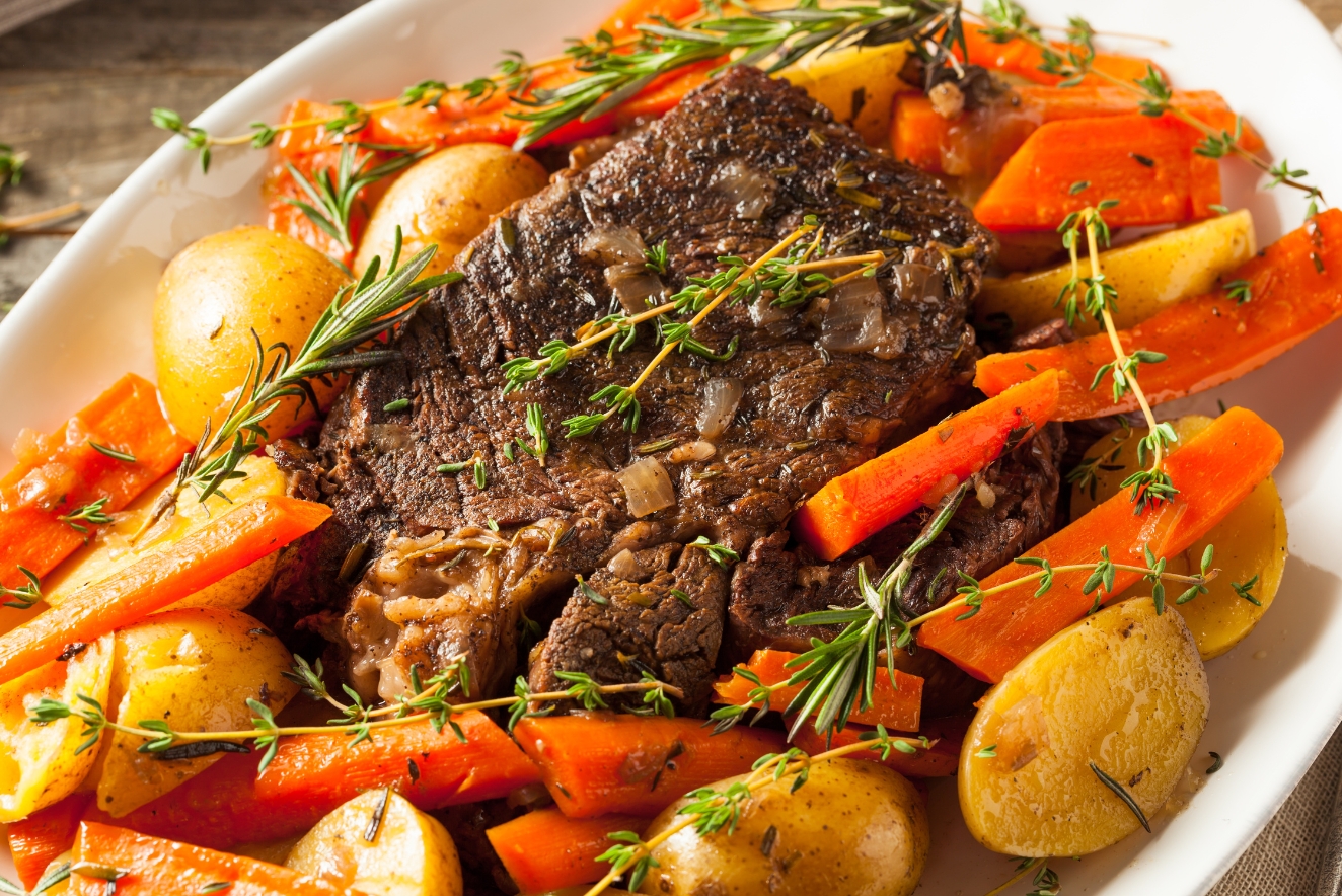 Tender pot roast with colorful roasted vegetables, including carrots and potatoes, garnished with fresh herbs on a white plate, showcasing hearty comfort food