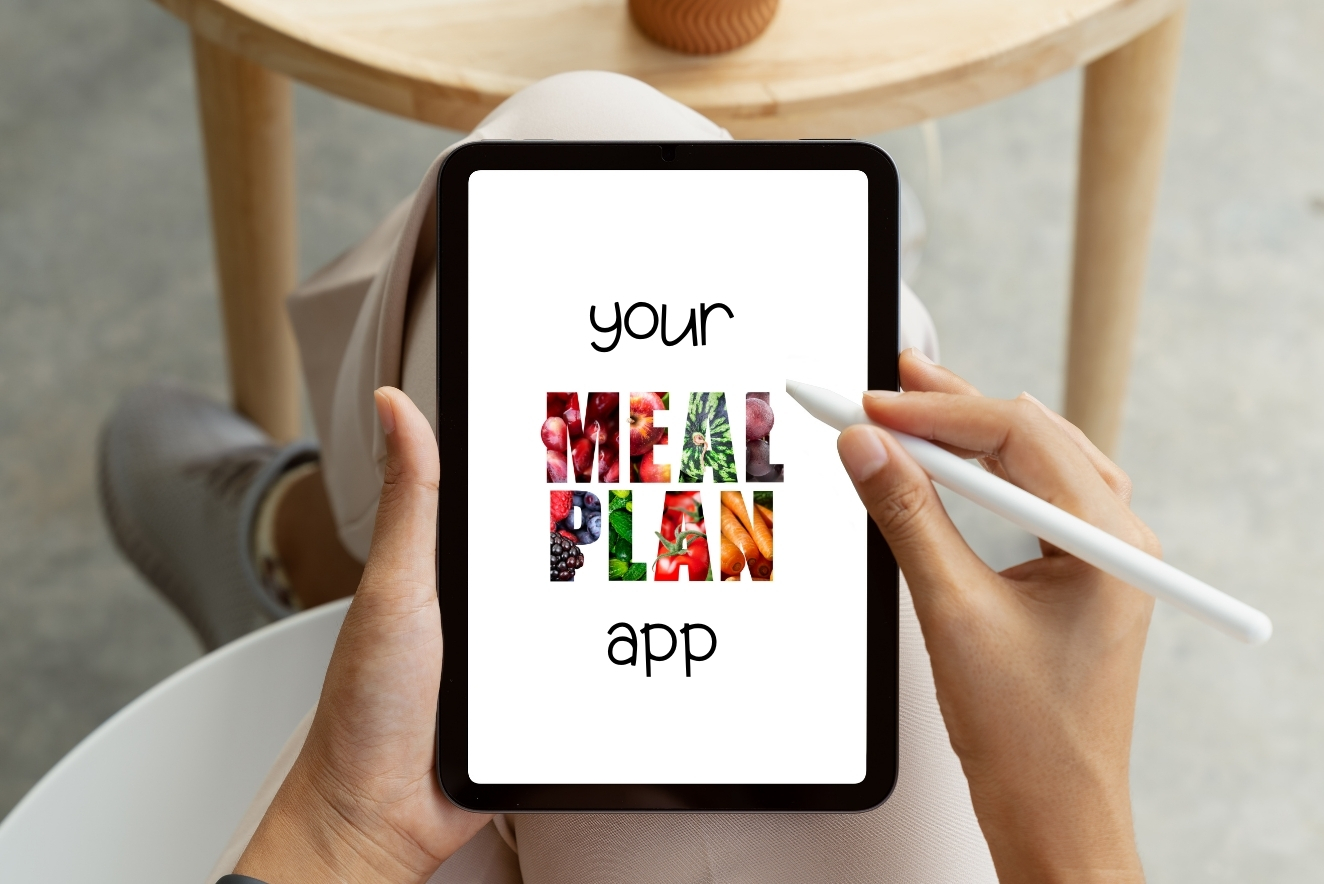 Hands holding a tablet with "Your MEAL PLAN app" displayed on the screen. The words "MEAL PLAN" are filled with colorful images of various foods. A stylus is being used to interact with the app.