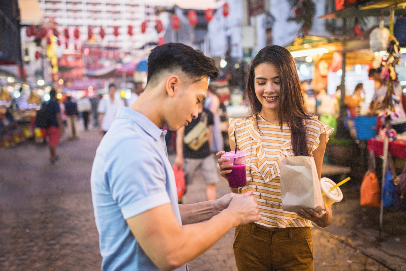 Budget travel experience: Tourists enjoying local street food at a bustling outdoor market, illustrating affordable culinary adventures.